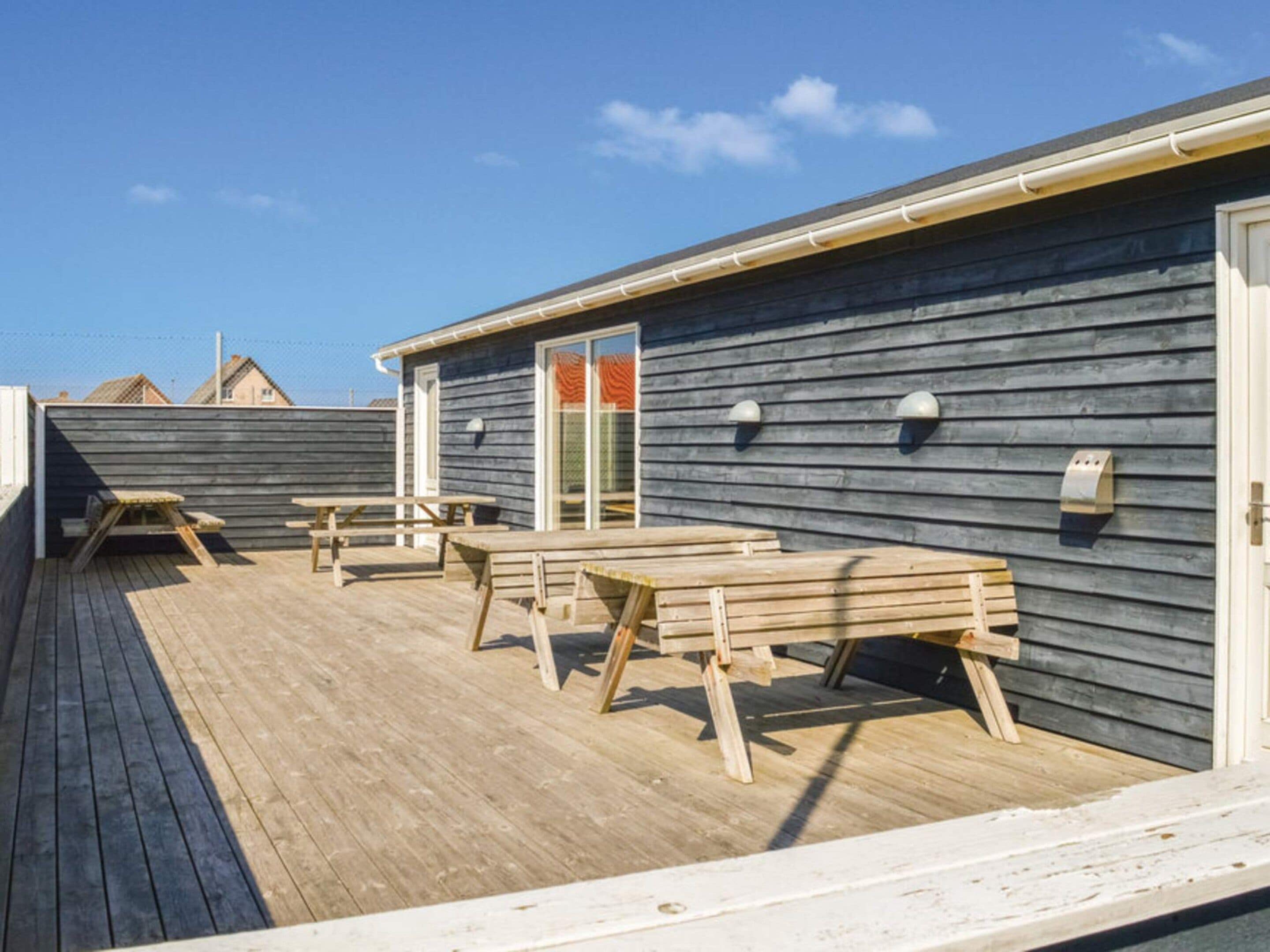 Eine Holzterrasse mit Picknicktischen und einem überdachten Bereich, wahrscheinlich eine Terrasse oder ein Sitzbereich im Freien.