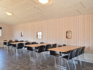 A conference room with multiple tables and chairs, wooden panel walls, and a stone-tiled floor.