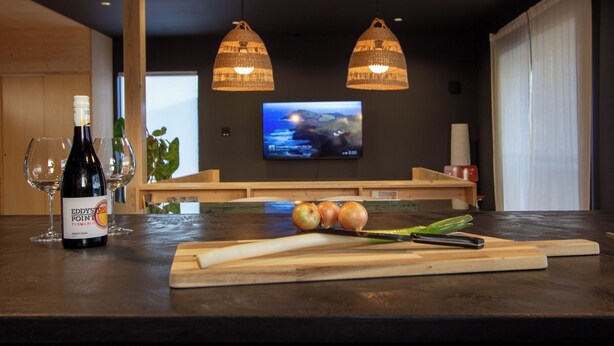 A restaurant interior with a counter, wine bottle, glasses, onions, and a TV on the wall.