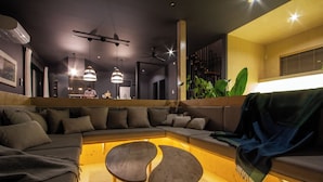 A modern living room with a sectional sofa, two wooden side tables, pendant lighting, and a large plant.
