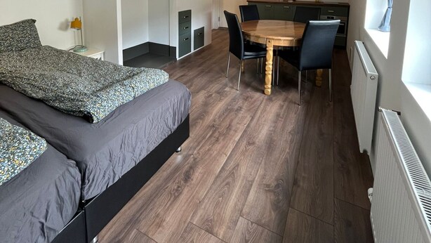 A compact room with a bed, a small kitchenette, a dining table with chairs, and a window.