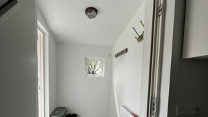 A narrow hallway with a tiled floor, a radiator, a trash bin, and a small window with a view of trees.