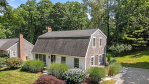 A single-story house with a gabled roof, surrounded by a well-maintained lawn and various shrubs. - The Horseshoe Crib; Minutes to Beach & Downtown (Sandwich)