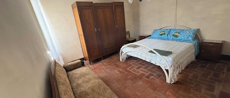 A bedroom with a bed, a wooden wardrobe, a bench, and a chandelier.