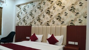 A hotel room with a large bed, two red pillows, a wooden headboard, and a floral wallpaper design. - RAGHAVAM (Faizabad)
