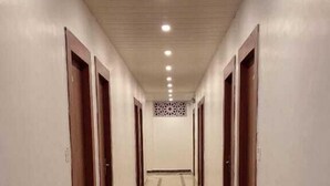 A long, narrow hallway with a reflective floor and evenly spaced doors on both sides. - RAGHAVAM (Faizabad)