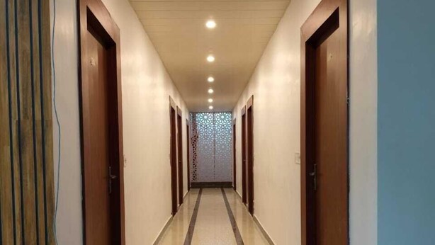 A hotel hallway with a central decorative wall, wooden doors, and a tiled floor. - RAGHAVAM (Faizabad)