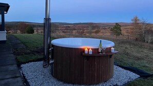 Un jacuzzi con revestimiento de madera, rodeado de grava, con vistas a las colinas al fondo.