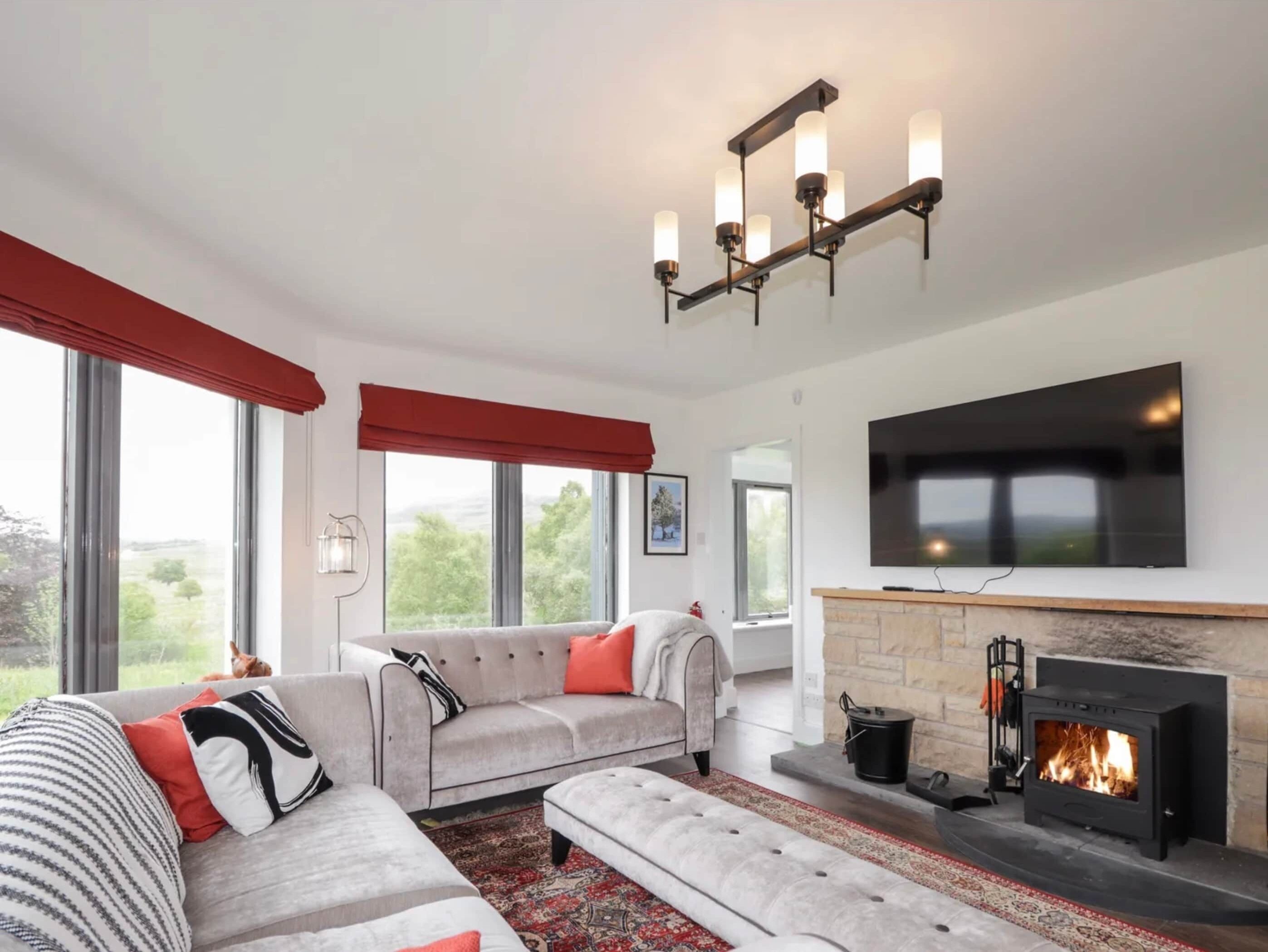 A modern living room with a fireplace, a large flat-screen TV, and a sofa with red cushions.