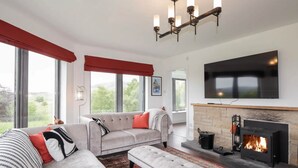 A modern living room with a fireplace, a large flat-screen TV, and a sofa with red cushions. - The Challenger Estate - Lodge (Lairg)