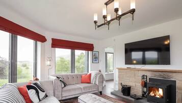 A modern living room with a fireplace, a large flat-screen TV, and a sofa with red cushions.
