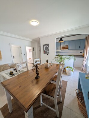A dining area with a wooden table, chairs, and a statue centerpiece. There is a kitchen in the background with blue cabinets and a hanging light fixture. - 202 - Livingtarifa Dolce Vita (Tarifa)
