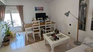 A well-lit living room with a TV, a coffee table with toys, a bed with pillows, and a painting of a building. - 202 - Livingtarifa Dolce Vita (Tarifa)