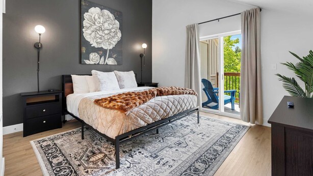 A modern bedroom with a bed, a nightstand, a wall-mounted lamp, and a large window with curtains.