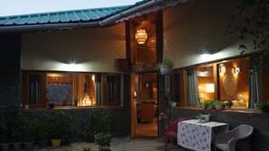 A cozy outdoor seating area with a table and chairs, surrounded by potted plants and a stone pathway. - The Whispering Pines (Dhari)