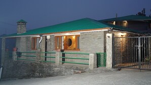 A stone building with a green roof, a wooden door, and a metal gate. - The Whispering Pines (Dhari)
