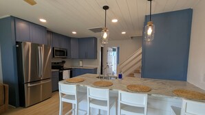 Une cuisine moderne dotée d’un îlot central, de tabourets de bar blancs, d’appareils électroménagers en acier inoxydable et de meubles de rangement bleus.