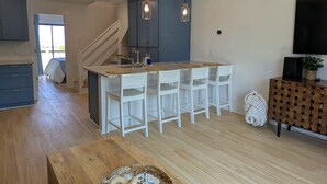 Une cuisine moderne dotée d’un îlot central, de tabourets de bar blancs, d’un éclairage suspendu et d’un escalier menant à un autre niveau.
