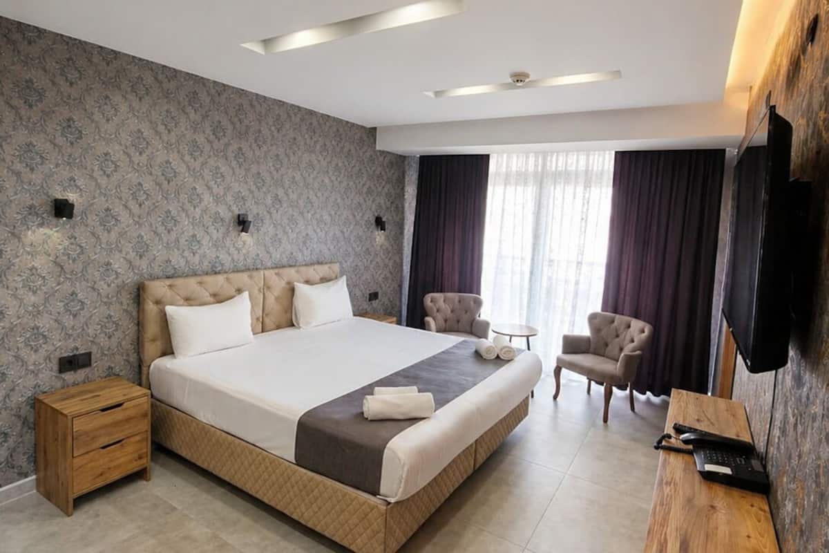 A modern hotel room with a large bed, a wooden nightstand, a desk, and a TV mounted on the wall.