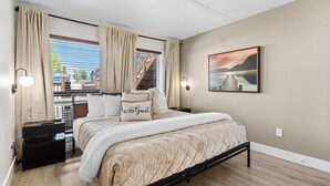 Un dormitorio con cama, cortinas, mesita de noche, lámpara de pared y un cuadro.