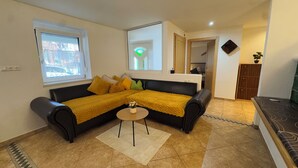 A living room with a black leather sofa, yellow throw blankets, a small round table with a vase, and a window with a view of the outside. - Vacation apartment Annemarie (Tirol)