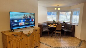 A dining area with a TV displaying various streaming services, a wooden cabinet, a table with chairs, and a window with a view of the outside. - Vacation apartment Annemarie (Tirol)