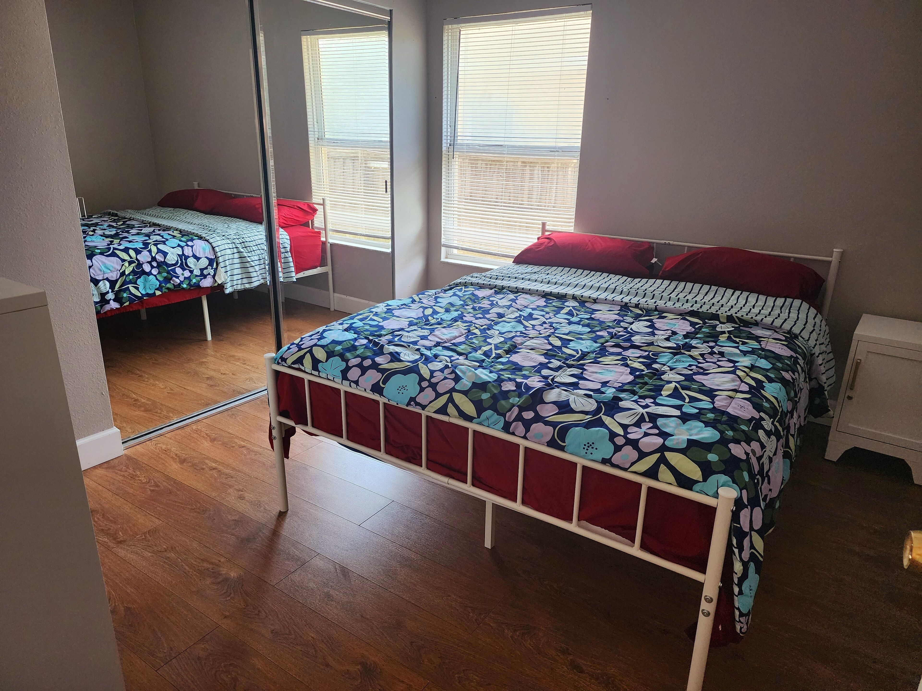 Un dormitorio con cama, mesita de noche, espejo y ventana con persianas.