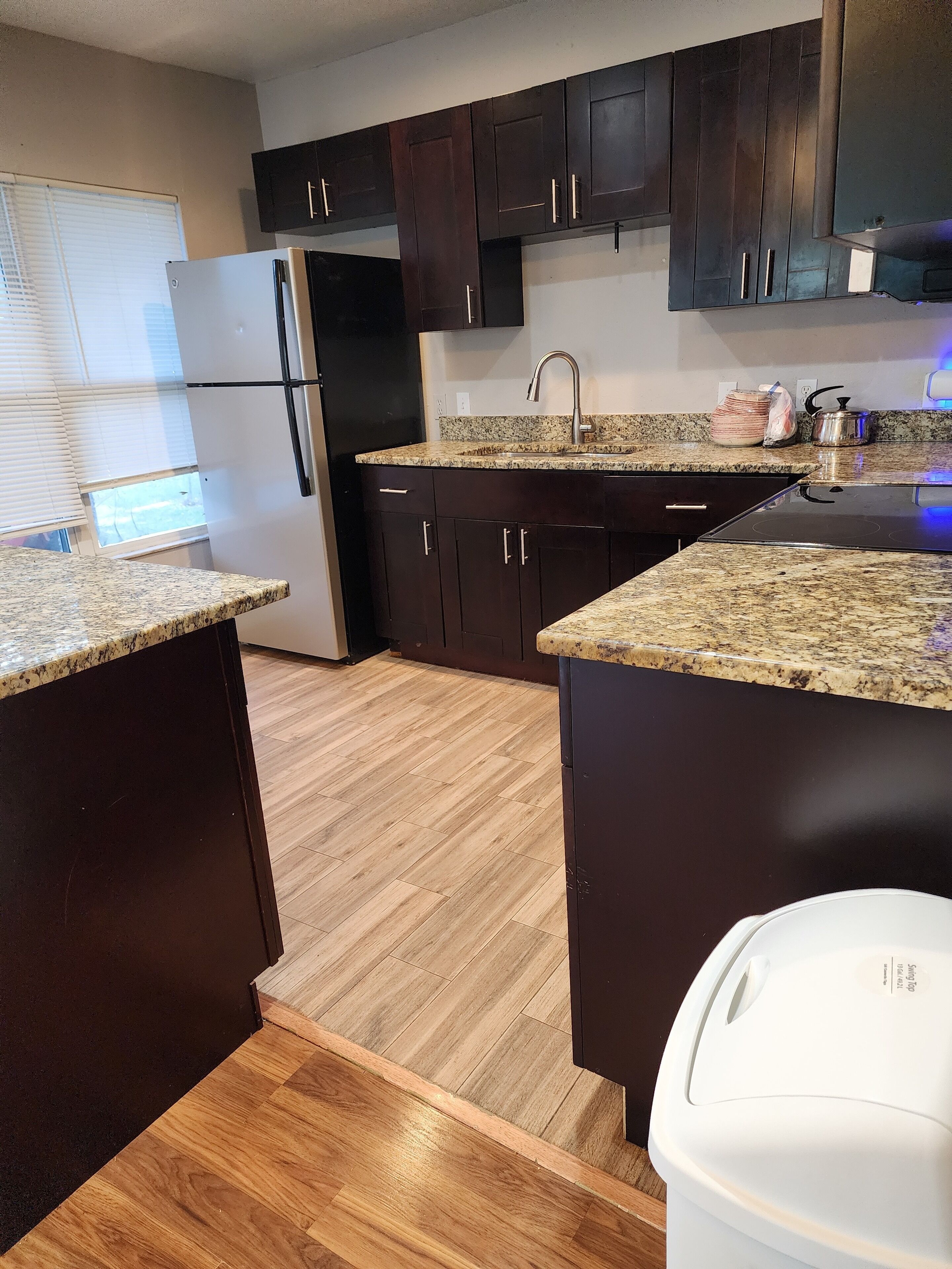 A kitchen with dark cabinets, a stainless steel refrigerator, a granite countertop, and a built-in stove.