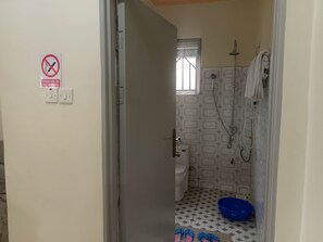 A small bathroom with a shower, toilet, and a blue basin. There is a no-smoking sign on the wall.