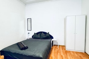 Un dormitorio con una cama, un armario blanco, una pequeña silla blanca y un cuadro en la pared.