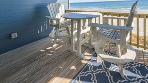 Een terras met Adirondack-stoelen en een tafel, met uitzicht op de oceaan.