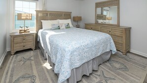 Een slaapkamer met een groot bed, een dressoir, een nachtkastje, een raam met uitzicht en een spiegel.