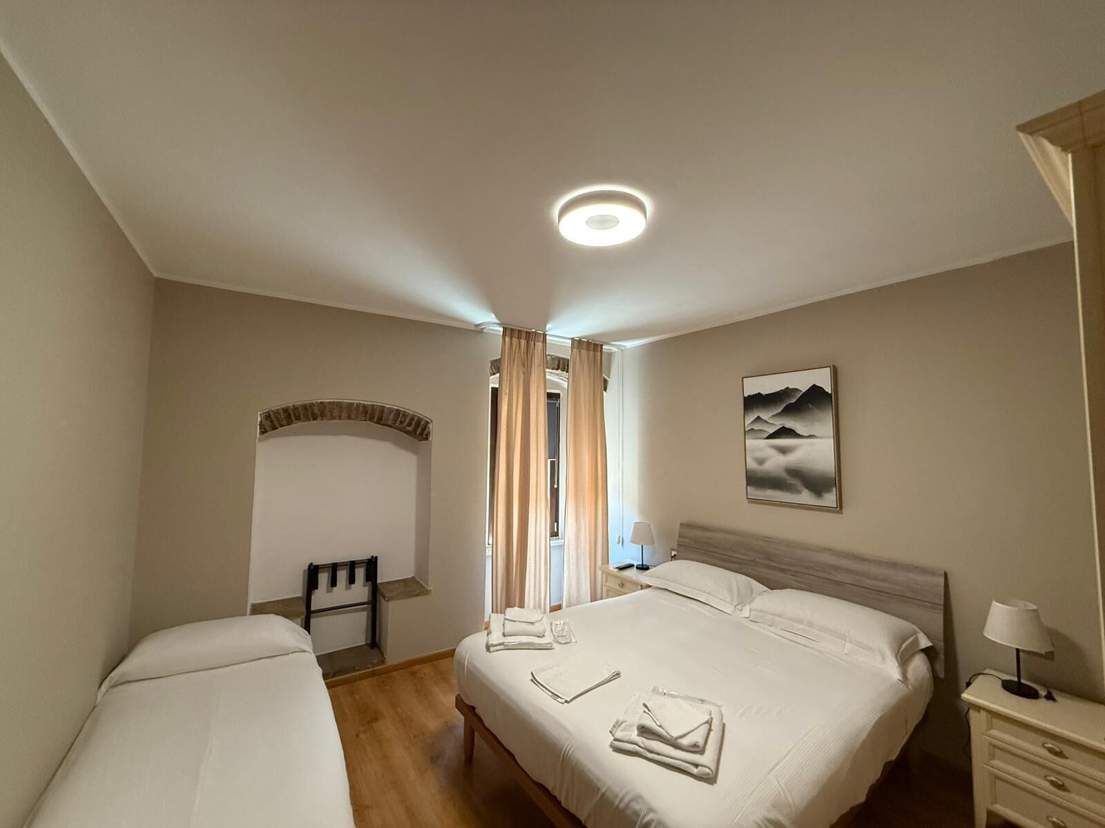A hotel room with two beds, a desk, a chair, a lamp, and a painting on the wall.