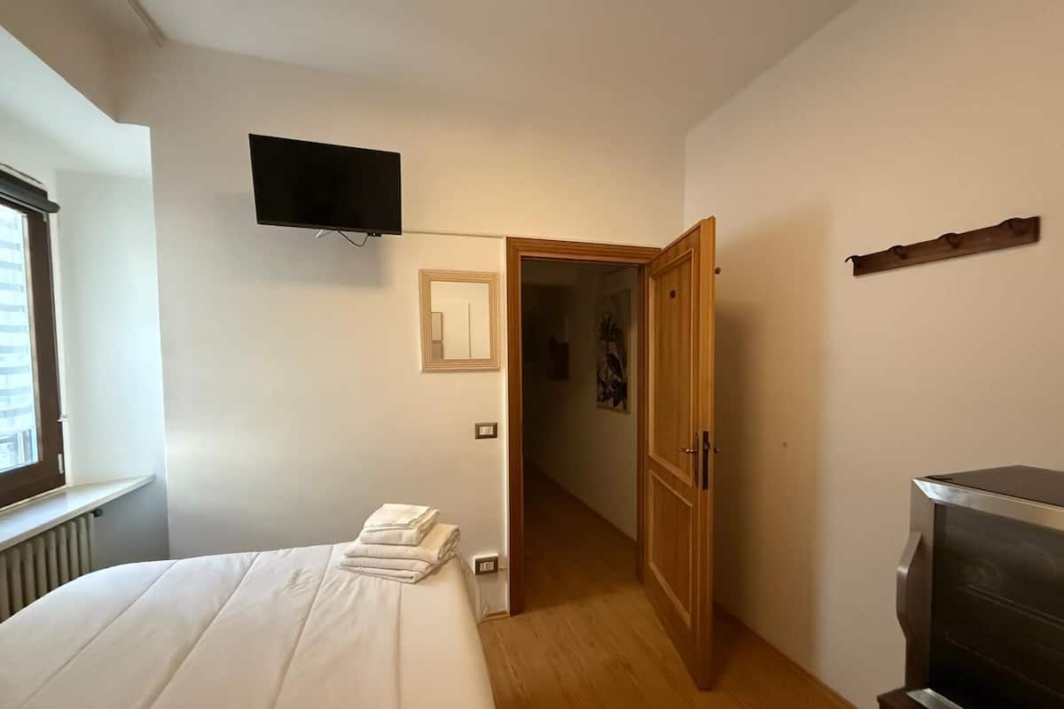 A bedroom with a bed, a TV mounted on the wall, a wooden door, and a radiator.
