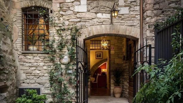 A stone building with an arched entrance, potted plants, and a hanging light fixture. - Hotel Lieto Soggiorno (Assisi)