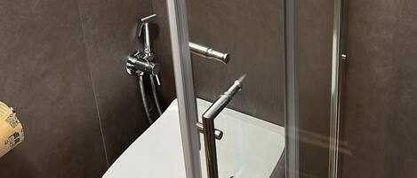 Un baño moderno con cabina de ducha de vidrio, un lavabo blanco y un panel de control en la pared.