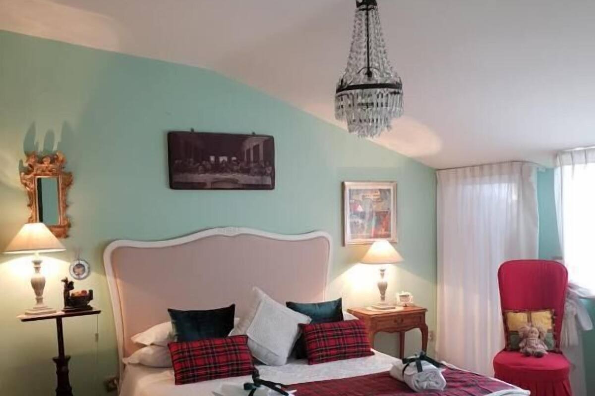 A neatly arranged bedroom with a large bed, two bedside tables with lamps, a red chair, and a chandelier.