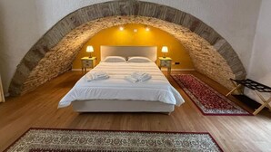 A bedroom with a stone arch ceiling, a bed with white linens, two bedside tables with lamps, and a red patterned rug. - Hotel Lieto Soggiorno (Assisi)