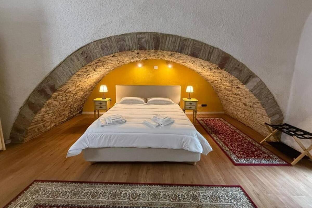 A bedroom with a stone arch ceiling, a bed with white linens, two bedside tables with lamps, and a red patterned rug.