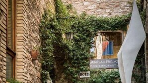 A stone building with a sign for a hotel and a minigallery. There are steps leading up to a seating area with a chair and a table. - Hotel Lieto Soggiorno (Assisi)