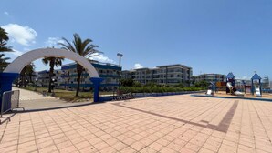 A paved walkway with a large archway, palm trees, and a playground with slides.
