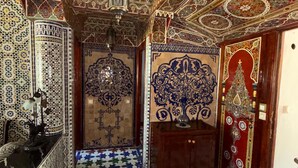 A room with intricate tile work on the walls and floor, a chandelier, and a wooden cabinet.