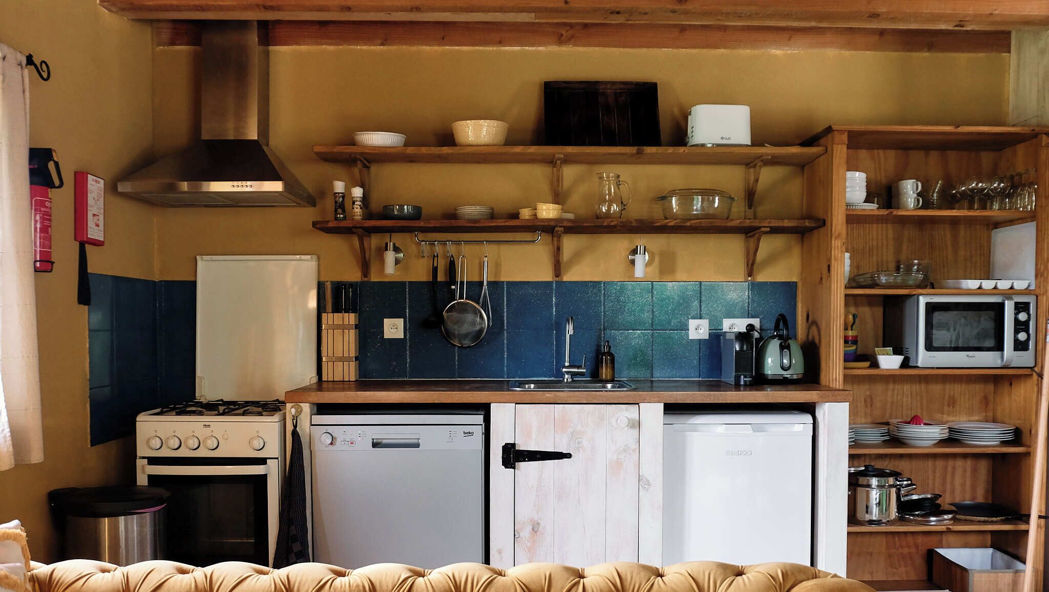 A compact kitchen with a gas stove, a dishwasher, a microwave, and wooden shelves above the counter.