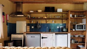 A compact kitchen with a gas stove, a dishwasher, a microwave, and wooden shelves above the counter.