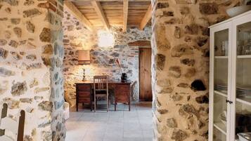 A stone-walled room with a wooden desk, chair, and a cabinet with glass doors.