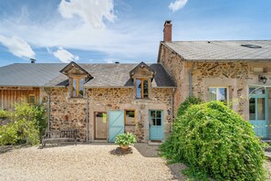 A stone building with a gravel driveway, a bench, and a large bush. - La vallée des Elements (Chiddes)