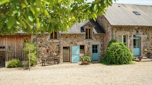 A stone building with a gravel driveway, wooden benches, and potted plants. - La vallée des Elements (Chiddes)