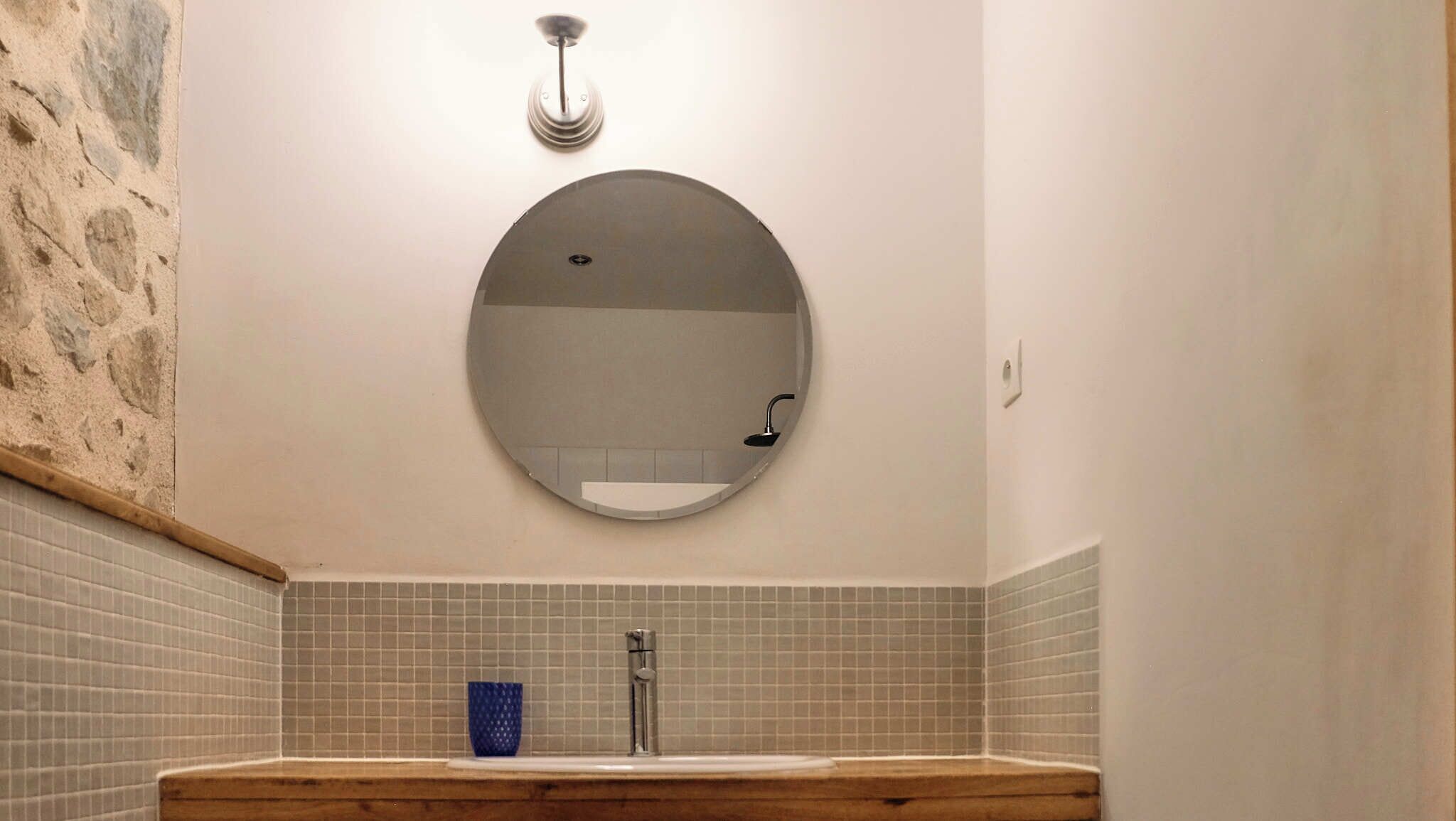A bathroom with a round mirror, a sink, and a shower.