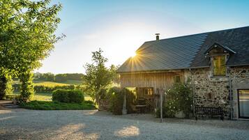 A stone house with a gravel driveway, a wooden bench, and a garden area.
