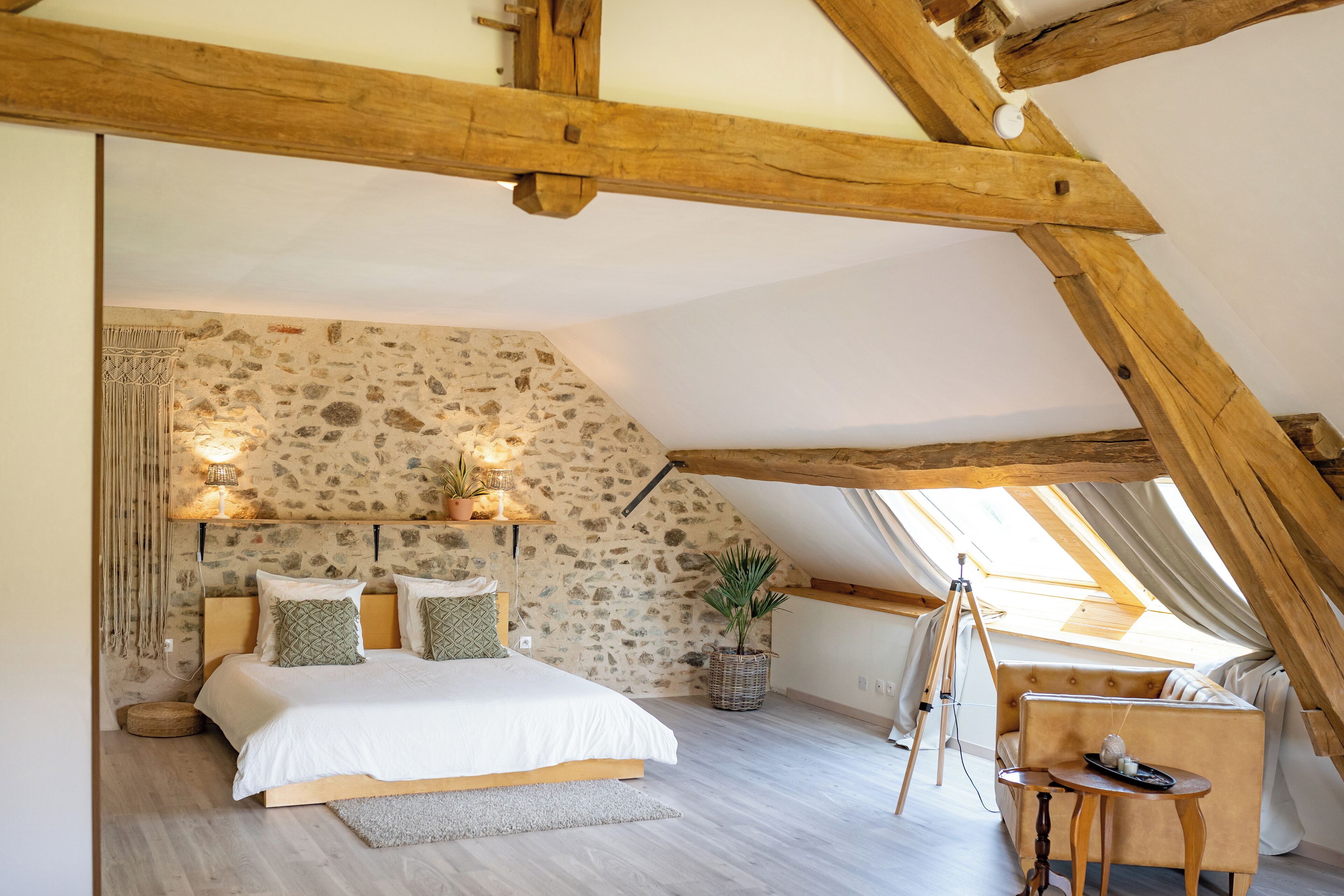 Une chambre avec un plafond en pente, un mur en pierre, un lit avec des oreillers, une petite table et une chaise.